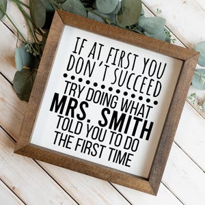Könnte beinhalten: Ein quadratisches Holzschild mit einem dunkelbraunen Rahmen und einem weißen Hintergrund. Das Schild zeigt schwarzen Text mit der Aufschrift: IF AT FIRST YOU DON'T SUCCEED TRY DOING WHAT MRS. SMITH TOLD YOU TO DO THE FIRST TIME. Der Text ist serifenlos.