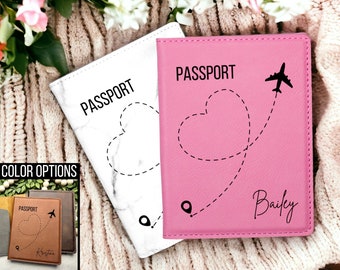 May include: Two passport covers with a heart and airplane design. One cover is white with a marble pattern and the other is pink with the name "Bailey". Both covers have the word "PASSPORT" printed on them.