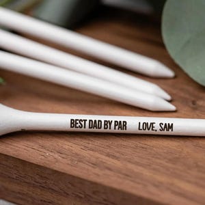 May include: White golf tees with a personalized message that reads "Best Dad By Par Love, Sam".
