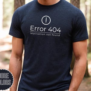 May include: A dark blue t-shirt with a white exclamation point icon and the text "Error 404 Motivation not found".