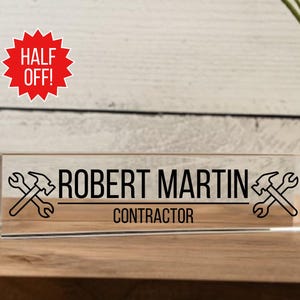 May include: A clear acrylic desk nameplate with the text "ROBERT MARTIN CONTRACTOR" and two crossed wrench and hammer icons.