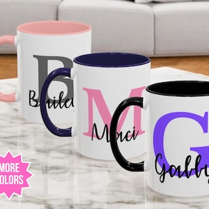 May include: Three personalised coffee mugs with black, pink and blue rims. The mugs are white with a large initial and a name printed in black below. The names are "Briley", "Merci", and "Gabby".