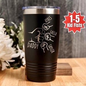 May include: Black insulated tumbler with a silver rim and lid. The tumbler features a graphic of a fist bump with the word "DADDY" and the names "AYRES", "LAELA", and "TAYLOR". A red starburst graphic reads "1-5 Kid Fists".