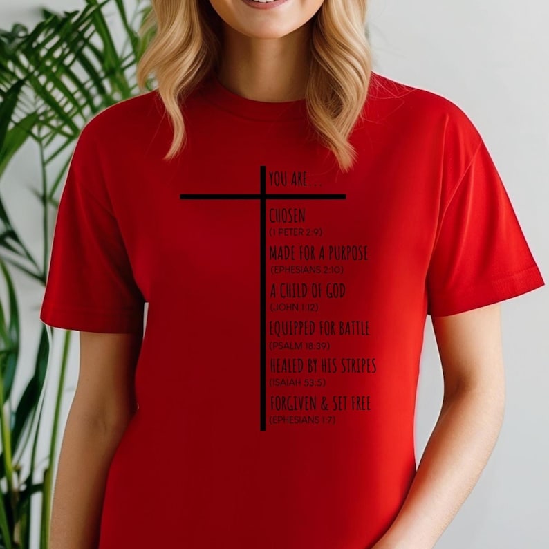 May include: Red t-shirt with a black cross and the text "You are... Chosen (1 Peter 2:9) Made for a Purpose (Ephesians 2:10) A Child of God (John 1:12) Equipped for Battle (Psalm 18:39) Healed by His Stripes (Isaiah 53:5) Forgiven & Set Free (Ephesians 1:7)"