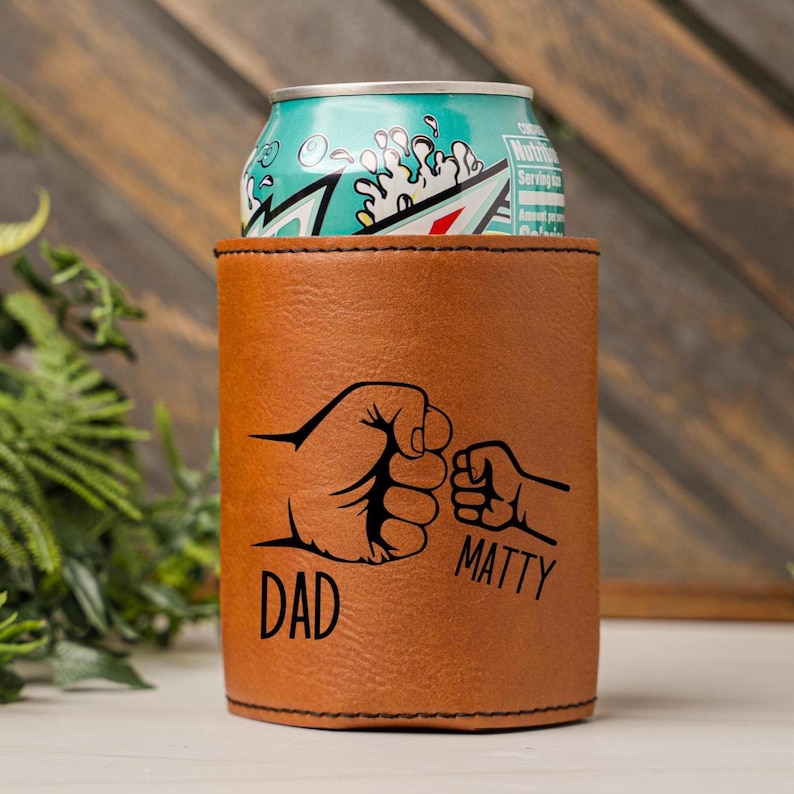 May include: Brown leather can cooler with a black design of two fists bumping. The text "DAD" is under the larger fist and "MATTY" is under the smaller fist.