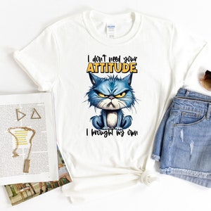 Op de afbeelding: Wit T-shirt met een blauwe cartoonkat en de tekst "Ik heb je houding niet nodig, ik heb mijn eigen".