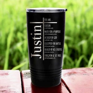 May include: Black insulated tumbler with the name "Justin" in white vertical text. The tumbler features a cross and inspirational text: "Chosen," "Made for a Purpose," "A Child of God," "Equipped for Battle," "Healed by His Stripes," and "Forgiven & Set Free."