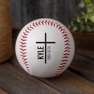 May include: White baseball with red stitching and a black cross with the name "KYLE" and the date "10.25.1995" printed on it.