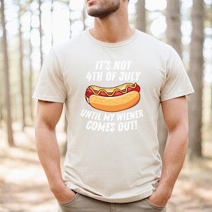 Pode incluir: Uma camiseta bege com um gr&aacute;fico branco de um cachorro-quente e o texto "N&atilde;o &eacute; 4 de julho at&eacute; que meu salsicha saia!"