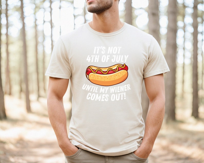 Pode incluir: Uma camiseta bege com um gr&aacute;fico branco de um cachorro-quente e o texto "N&atilde;o &eacute; 4 de julho at&eacute; que meu salsicha saia!"