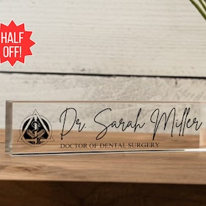 May include: A clear acrylic desk nameplate with a black and gold dental symbol, the text "Dr. Sarah Miller" and the words "Doctor of Dental Surgery".