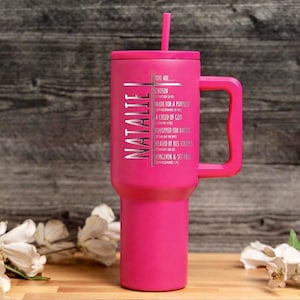May include: A vibrant pink tumbler with a handle and a matching lid, featuring a silver cross design and the name "NATALIE". The tumbler includes the text "YOU ARE..." followed by inspirational phrases. A pink straw is inserted in the lid.