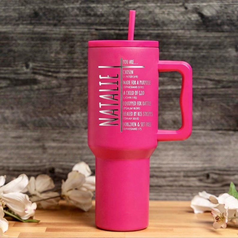 May include: A vibrant pink tumbler with a handle and a matching lid, featuring a silver cross design and the name "NATALIE". The tumbler includes the text "YOU ARE..." followed by inspirational phrases. A pink straw is inserted in the lid.