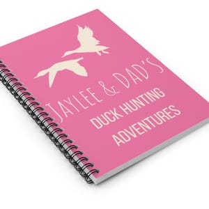 May include: Pink spiral bound notebook with the text "Jaylee & Dad's Duck Hunting Adventures" in white. The notebook features two white silhouettes of ducks flying.