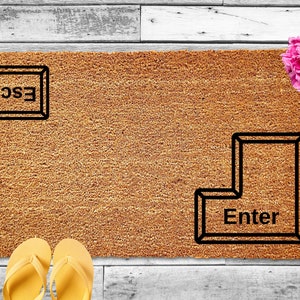 May include: A brown doormat with the words "ESC" and "Enter" printed on it in black. The doormat is made of a textured material and has a rectangular shape.