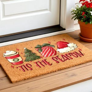 K&ouml;nnte beinhalten: Eine rechteckige Fu&szlig;matte mit festlichem Design. Sie zeigt eine Kaffeetasse, einen Weihnachtsbaum, ein Geschenk und einen Weihnachtsm&uuml;tze mit den Worten "'Tis the Season" in Rot. Die Matte besteht aus Naturfasermaterial.