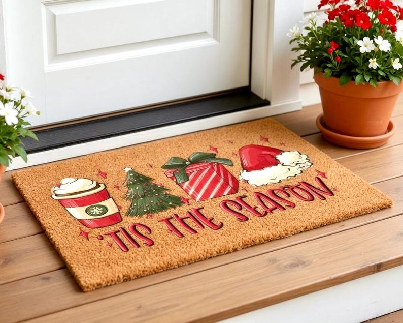 K&ouml;nnte beinhalten: Eine rechteckige Fu&szlig;matte mit festlichem Design. Sie zeigt eine Kaffeetasse, einen Weihnachtsbaum, ein Geschenk und einen Weihnachtsm&uuml;tze mit den Worten "'Tis the Season" in Rot. Die Matte besteht aus Naturfasermaterial.