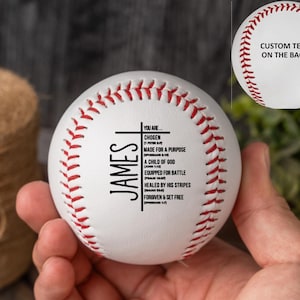 May include: A white baseball with red stitching and the text "JAMES" vertically. The ball has inspirational text including "CHOSEN" and "MADE FOR A PURPOSE." The words "CUSTOM TEXT ON THE BACK" are also visible.
