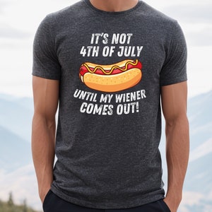 Pode incluir: Uma camiseta cinza escura com um gr&aacute;fico branco que diz "N&atilde;o &eacute; 4 de julho at&eacute; que meu salsicha saia!" e um desenho animado de um cachorro-quente com mostarda e ketchup.