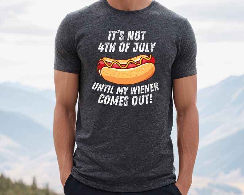 Pode incluir: Uma camiseta cinza escura com um gr&aacute;fico branco que diz "N&atilde;o &eacute; 4 de julho at&eacute; que meu salsicha saia!" e um desenho animado de um cachorro-quente com mostarda e ketchup.