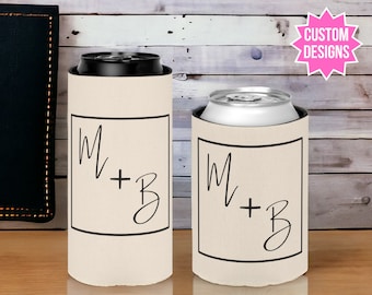 May include: Two beige can coolers with black trim and the text "M + B" in a handwritten font. The coolers are on a wooden surface.