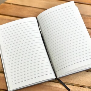 May include: A black lined notebook with a white cover and a black spine. The notebook is open to a blank page with lined paper.