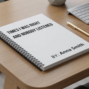 May include: A white spiral-bound notebook with the text "TIMES I WAS RIGHT AND NOBODY LISTENED" and "BY: Anna Smith" printed in black. A gold pen and keyboard are visible on a wooden desk.