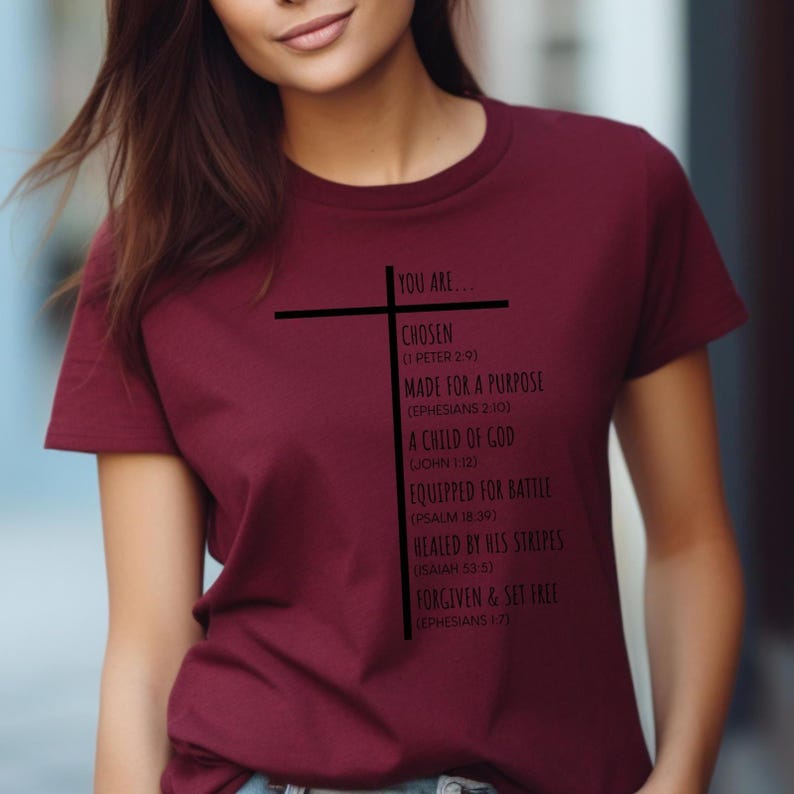May include: A maroon t-shirt with a black cross and text that reads "You are... Chosen (1 Peter 2:9) Made for a Purpose (Ephesians 2:10) A Child of God (John 1:12) Equipped for Battle (Psalm 18:39) Healed by His Stripes (Isaiah 53:5) Forgiven & Set Free (Ephesians 1:7)"