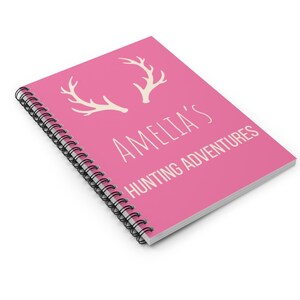 May include: Pink spiral bound notebook with white antlers and the text "Amelia's Hunting Adventures".