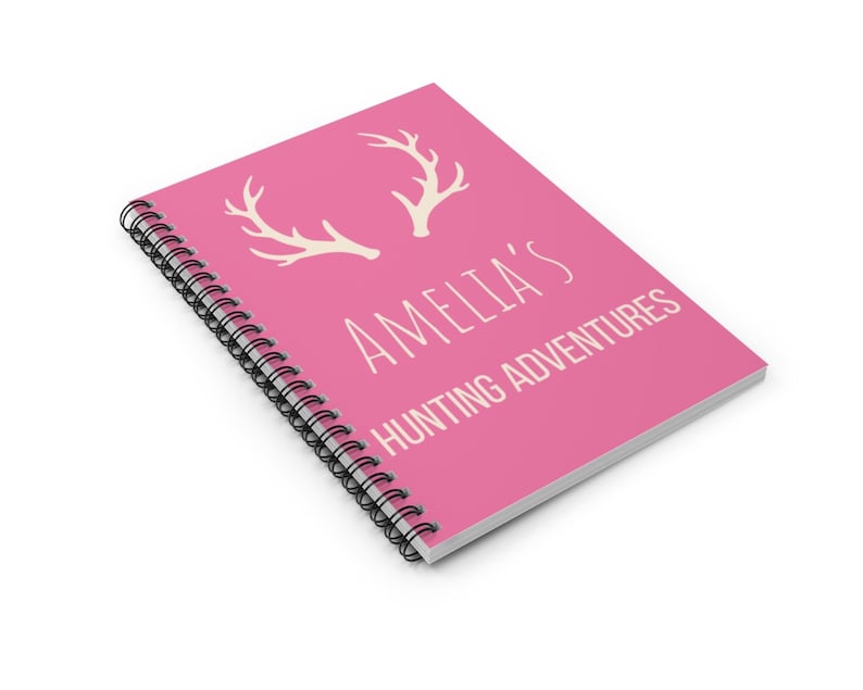 May include: Pink spiral bound notebook with white antlers and the text "Amelia's Hunting Adventures".