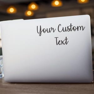 May include: A silver laptop computer with a black sticker that says "Your Custom Text" on the lid.