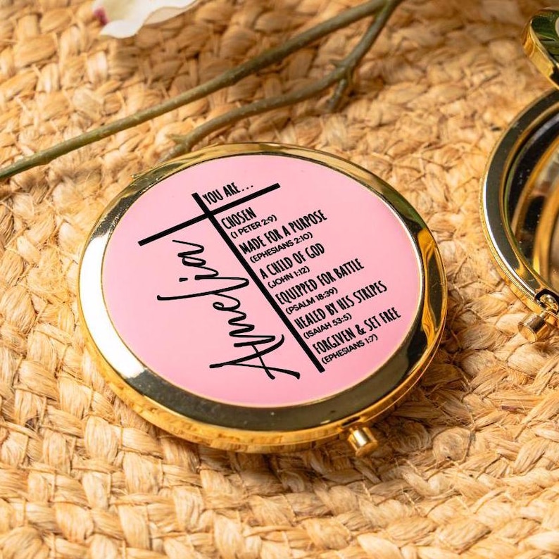 Peut inclure: Un miroir compact rose avec une bordure dor&eacute;e et le nom "Amelia" &eacute;crit en cursive noire. Le miroir a un motif de croix et des citations inspirantes avec des versets bibliques.
