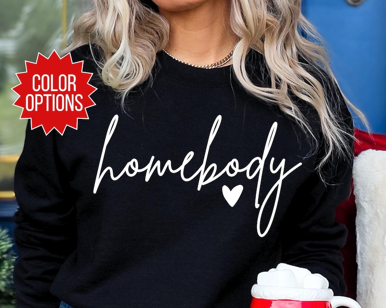 K&ouml;nnte beinhalten: Schwarzer Pullover mit wei&szlig;em Text, der "homebody" mit einem kleinen wei&szlig;en Herz sagt.