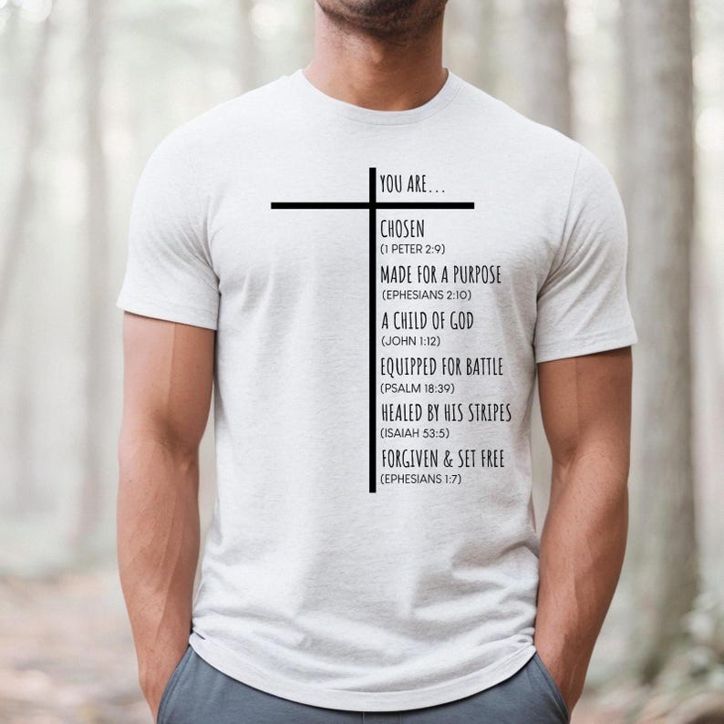 May include: A white t-shirt with a black cross and text that reads "You are... Chosen (1 Peter 2:9) Made for a Purpose (Ephesians 2:10) A Child of God (John 1:12) Equipped for Battle (Psalm 18:39) Healed by His Stripes (Isaiah 53:5) Forgiven & Set Free (Ephesians 1:7)"