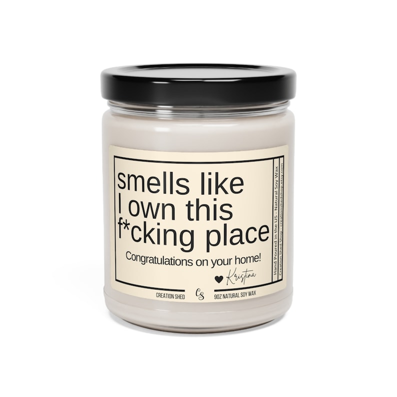 May include: A white candle jar with a black lid and a label that reads "smells like I own this f*cking place. Congratulations on your home!" The label also includes the text "Creation Shed" and "9oz Natural Soy Wax".
