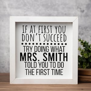 May include: A square wooden sign with a white frame and a white background featuring black text that reads: IF AT FIRST YOU DON'T SUCCEED TRY DOING WHAT MRS. SMITH TOLD YOU TO DO THE FIRST TIME. The sign has a clean, simple design.