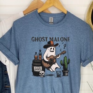 May include: A blue t-shirt with the text "Ghost Malone" printed on it. A cartoon ghost wearing a cowboy hat is playing a guitar and holding a bottle of "Cow Spirit".