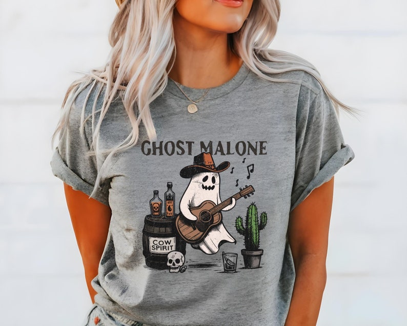 May include: A gray t-shirt with a graphic of a ghost playing a guitar and the text "Ghost Malone". The ghost is wearing a cowboy hat and there are bottles of "Cow Spirit" liquor in the background.