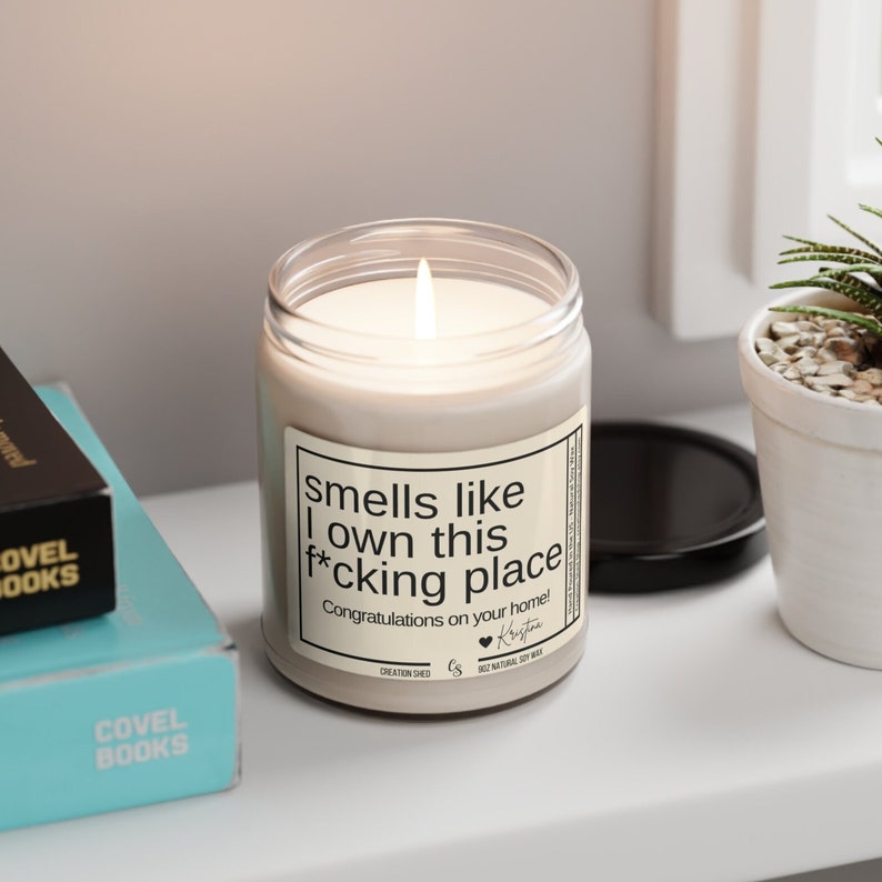 May include: A white candle in a glass jar with a black label that reads "Smells like I own this f*cking place. Congratulations on your home!" The label also includes a small heart and the name "Krista".