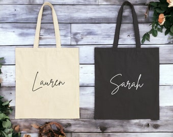 May include: Two tote bags, one beige and one black, with the names "Lauren" and "Sarah" written in cursive on the front.