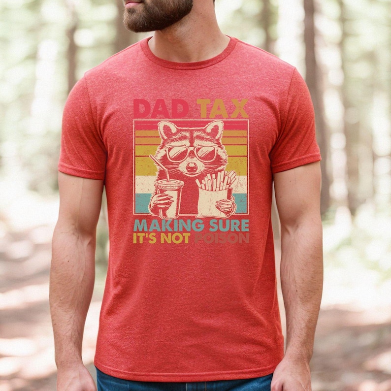 K&ouml;nnte beinhalten: Rotes T-Shirt mit einer Grafik eines Waschb&auml;ren mit Sonnenbrille, der ein Getr&auml;nk und Pommes h&auml;lt. Der Text auf dem Shirt lautet "DAD TAX MAKING SURE IT'S NOT POISON" im Retro-Stil. Das Shirt ist aus weichem Material.