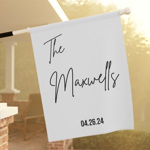 May include: White personalized house flag with black text that reads "The Maxwells 04.26.24".