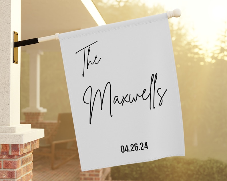 May include: White personalized house flag with black text that reads "The Maxwells 04.26.24".