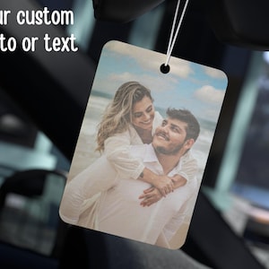 May include: Rectangular air freshener with a photo of a couple on a beach, hanging from a string. The air freshener has rounded corners and a small hole at the top. The text "your custom photo or text" is at the top left.