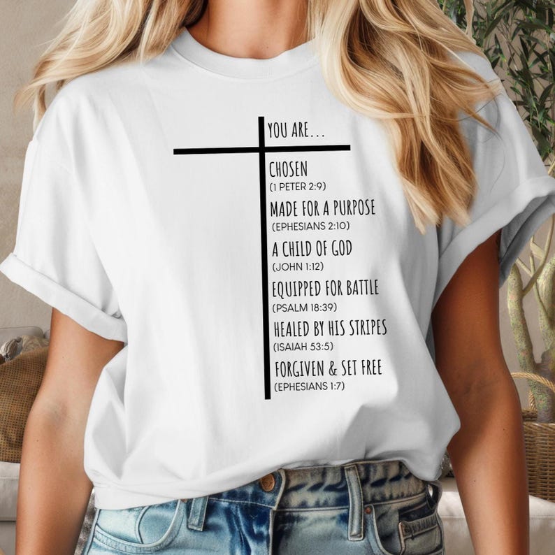 May include: White t-shirt with a black cross and text that reads "You are... Chosen (1 Peter 2:9) Made for a Purpose (Ephesians 2:10) A Child of God (John 1:12) Equipped for Battle (Psalm 18:39) Healed by His Stripes (Isaiah 53:5) Forgiven & Set Free (Ephesians 1:7)"