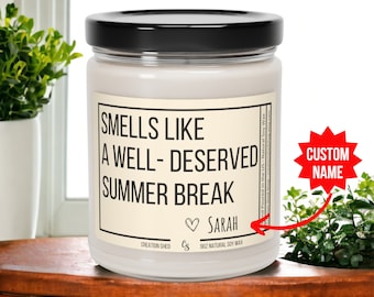 May include: A white candle jar with a black lid and a label that reads "Smells Like A Well-Deserved Summer Break" with a heart and the name "Sarah". The label also includes "Creation Shed" and "9oz Natural Soy Wax".