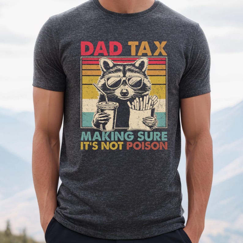 K&ouml;nnte beinhalten: Dunkelgraues T-Shirt mit einer Grafik eines Waschb&auml;ren mit Sonnenbrille, der ein Getr&auml;nk und Pommes h&auml;lt. Der Text lautet "DAD TAX MAKING SURE IT'S NOT POISON" im Retro-Stil.