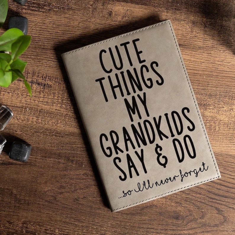 May include: A gray faux leather journal with the text "Cute Things My Grandkids Say & Do...so I'll never forget" printed in black.