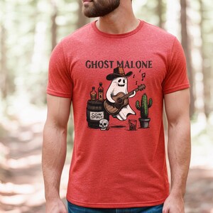 May include: Red t-shirt with a graphic of a ghost wearing a cowboy hat and playing a guitar. The text "Ghost Malone" is printed on the shirt.