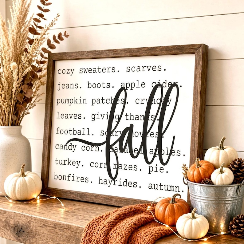 May include: A rectangular wooden framed sign with a white background featuring black text listing fall-themed words including cozy sweaters, scarves, jeans, boots, apple cider, pumpkin patches, crunchy leaves, giving thanks, football, scary movies, candy corn, caramel apples, turkey, corn mazes, pie, bonfires, hayrides, autumn, and the word fall in large script.